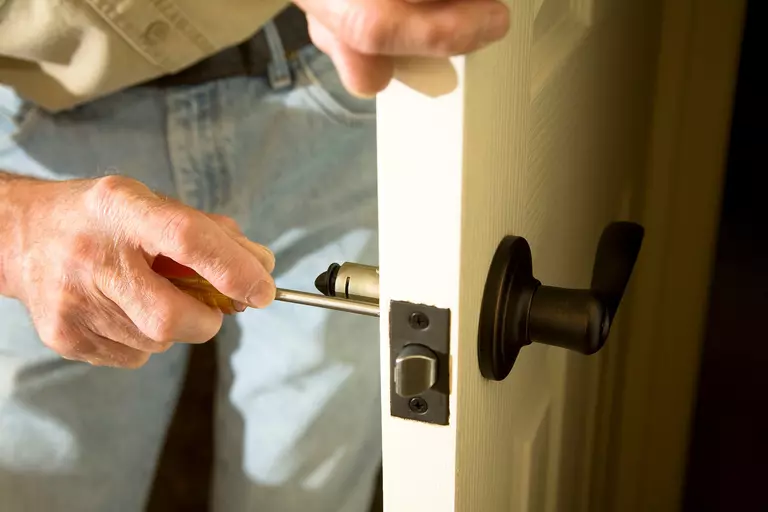 Close-up of hands holding a screwdriver, replacing the lock mechanism of an entry door.