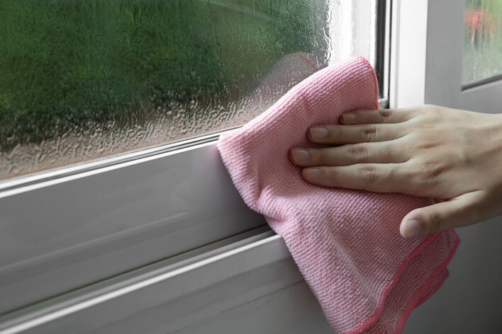 Person wiping condensation on windows inside their home with a pink cloth.