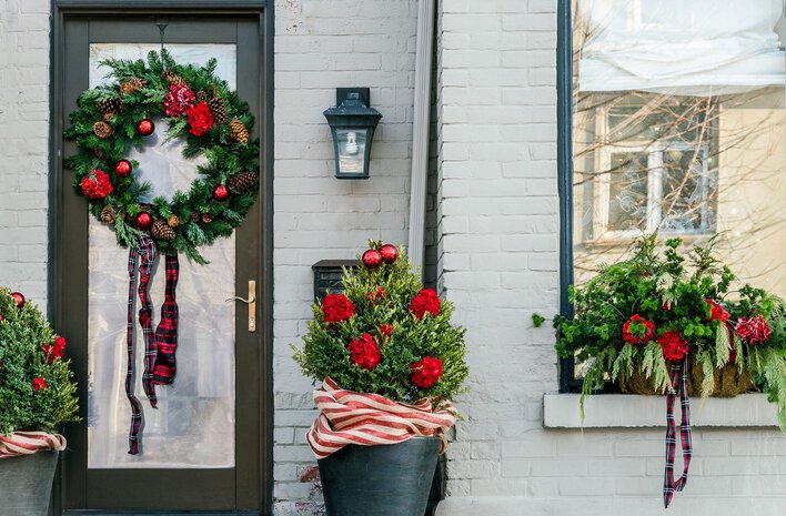 The entryway of a gray-colored house decorated for Christmas, including a wreath hung on the door.