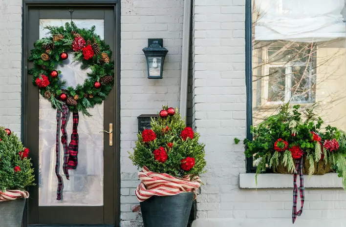 The entryway of a gray-colored house decorated for Christmas, including a wreath hung on the door.