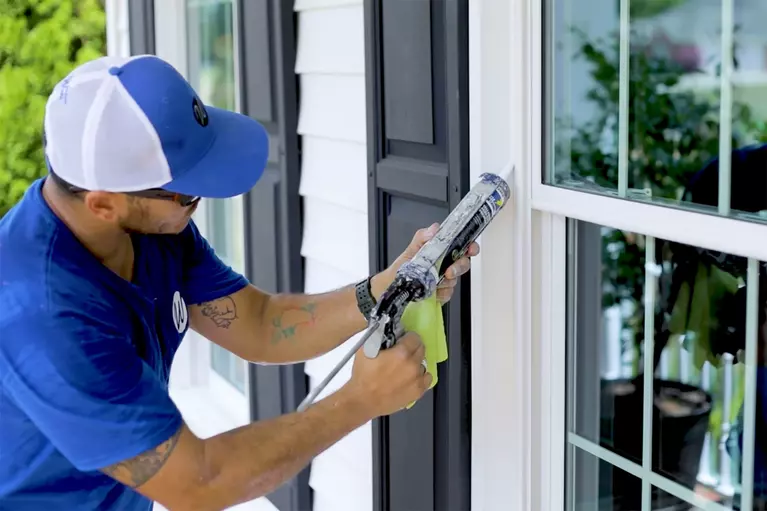 Window World employee applying caulk to a window on the exterior of a home.