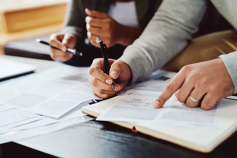 Two people inspecting documents on a table.