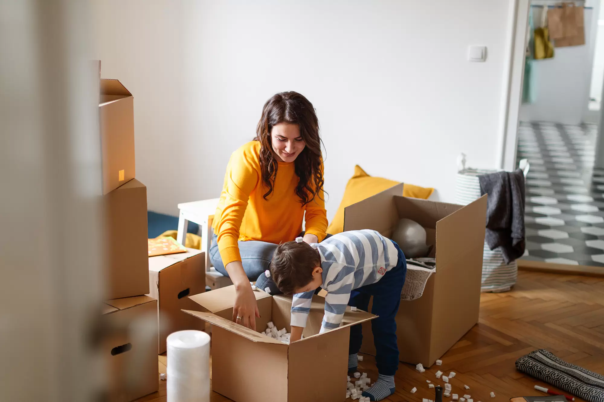 A mother and her child unpack cardboard boxes in a home.