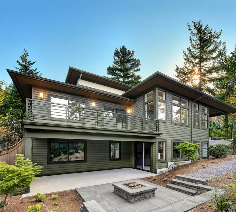 A modern home with green vinyl siding, flat architectural lines, and a fetching outdoor fireplace.