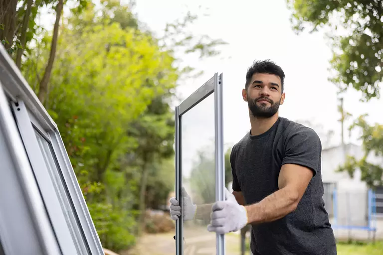 A man wearing protective gloves carrying a window.