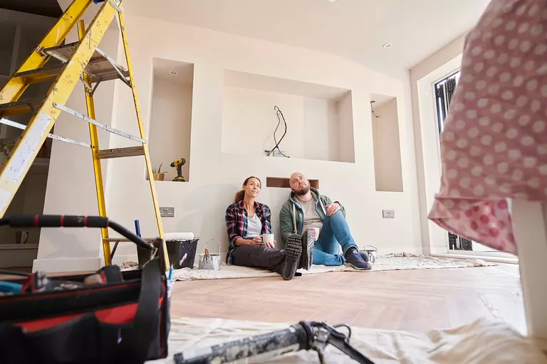 Couple sitting on floor of home taking a coffee break from home renovation.
