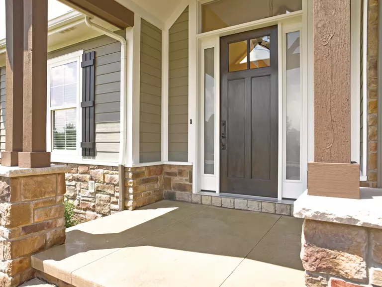 A brown fiberglass entry door on a vinyl siding and stone home with a small front porch leading into the home. 