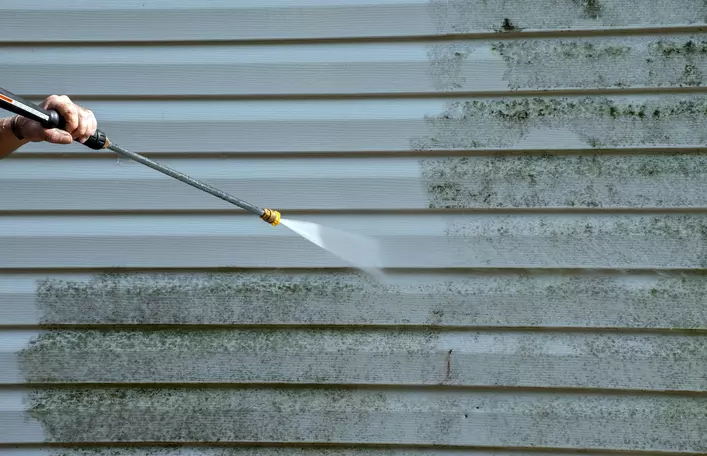 Person pressure washing vinyl siding on house