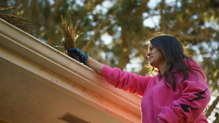 Woman cleaning leaves and debris from gutters on the roof of a home