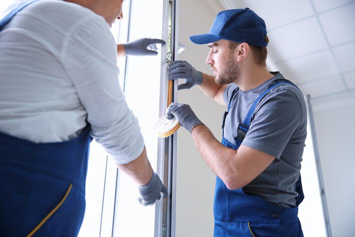Two men adding weatherstripping to an exterior door
