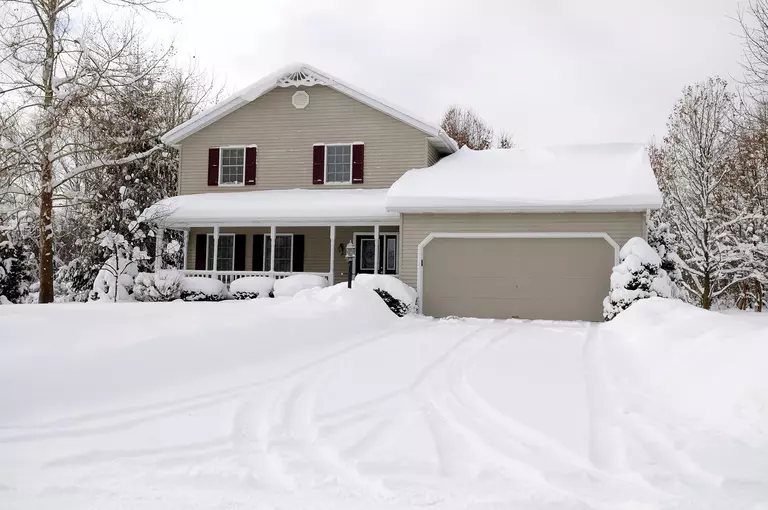 A gray siding home with a heavy layer of snow on the roof and all throughout the yard
and trees.