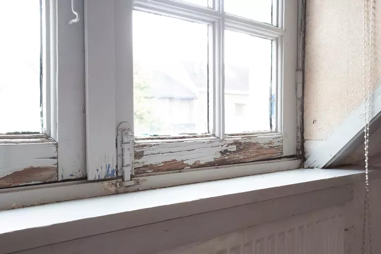 Old wooden window frames with rotting wood and cracked peeling paint as an indicator
of a house in need of renovation and new frames