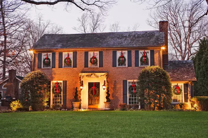 Exterior of a traditional brick home that is decorated for Christmas with ribbon-hung
wreaths on windows and doors and garland around the entryway.