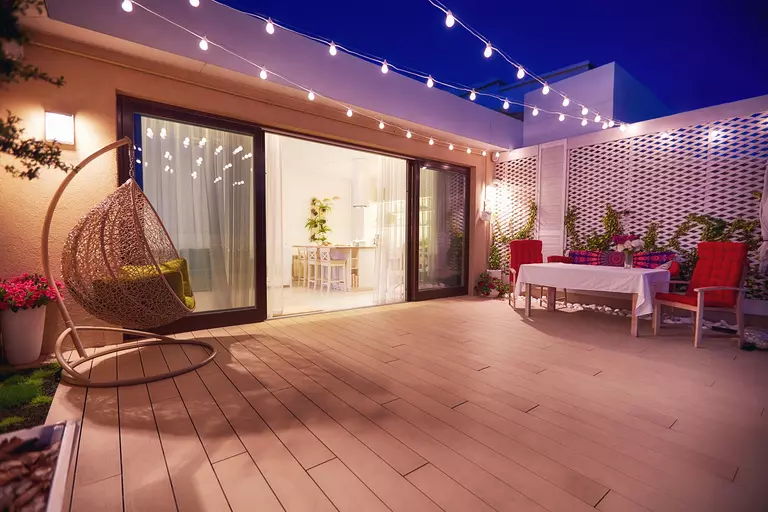Large sliding patio doors leading to a spacious back patio decorated with string lights and cozy outdoor furniture to make for a warm, welcoming outdoor gathering area. 