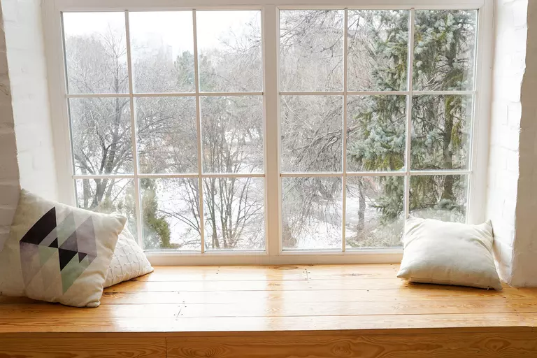 Window with a view of a winter landscape outside and a seating bench in front.