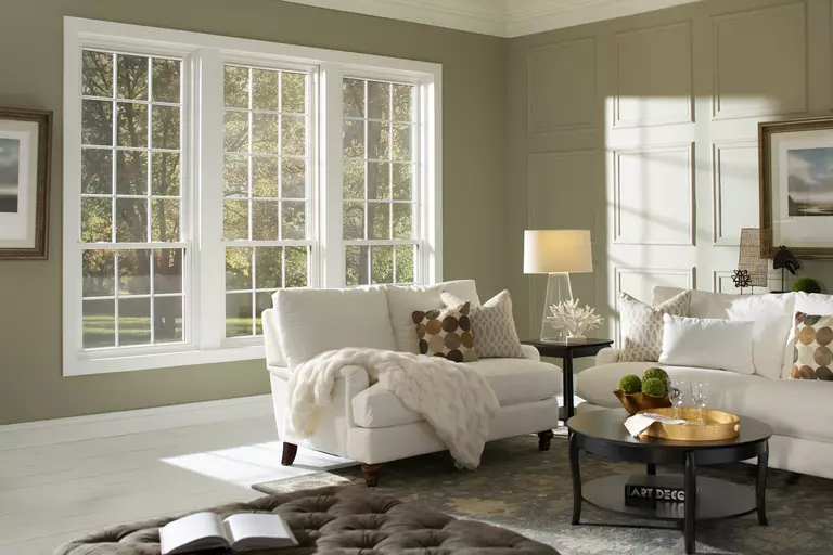 Living room with three double-hung windows looking out at trees.