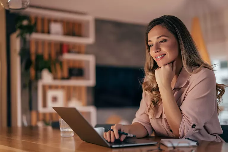Young woman sitting at a table while smiling at her laptop screen.