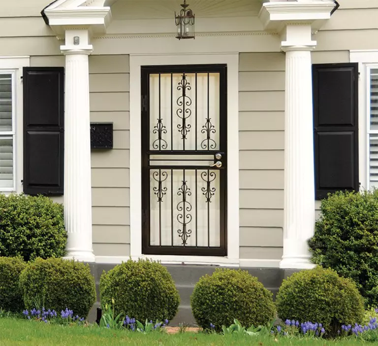 A security storm door with heavy iron construction on the front of a house with white decorative columns.