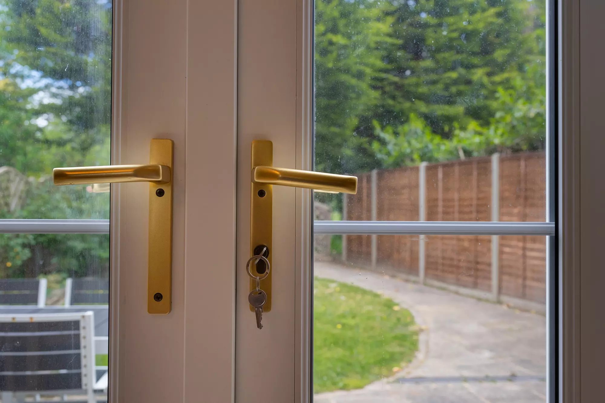 Close-up of handles of patio doors with back patio and garden in the background.