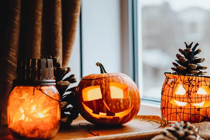 Halloween cozy mood composition with candles and jack-o’-lanterns on a windowsill. 