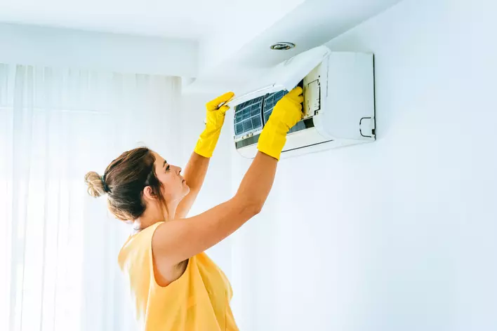 A woman changing the air filter on a split HVAC wall unit