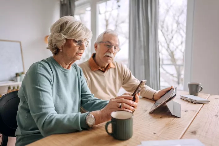 An older married couple sitting at their dining table in their renovated age-in-place home
enjoying coffee as they look on their smartphone.