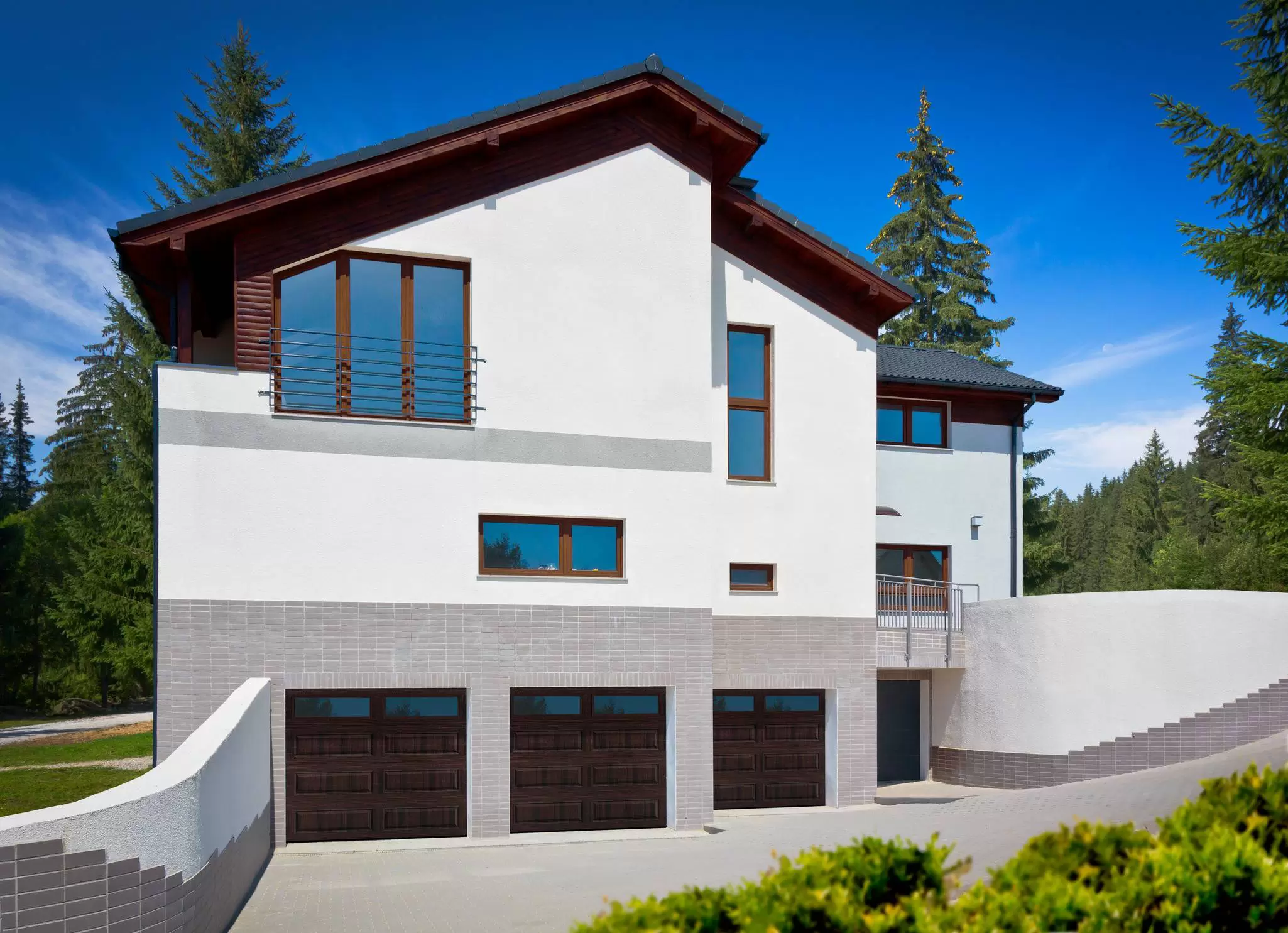 Modern-mountain home with dark wood-framed windows and garage doors surrounded by evergreen trees.