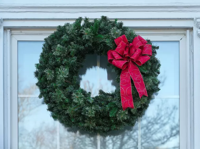 A wreath with a red bow hanging outside of a square window.