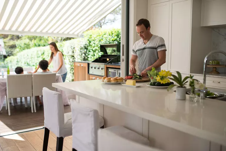Father preparing lunch for his family of four while they’re on the terrace of the outside living space.