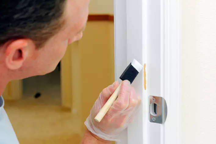 Person painting the side of a wall with a small paintbrush in hand
