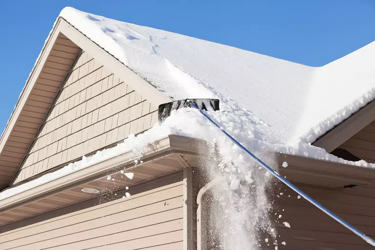 A roof rake being used to remove several inches of snow from the roof of a home.