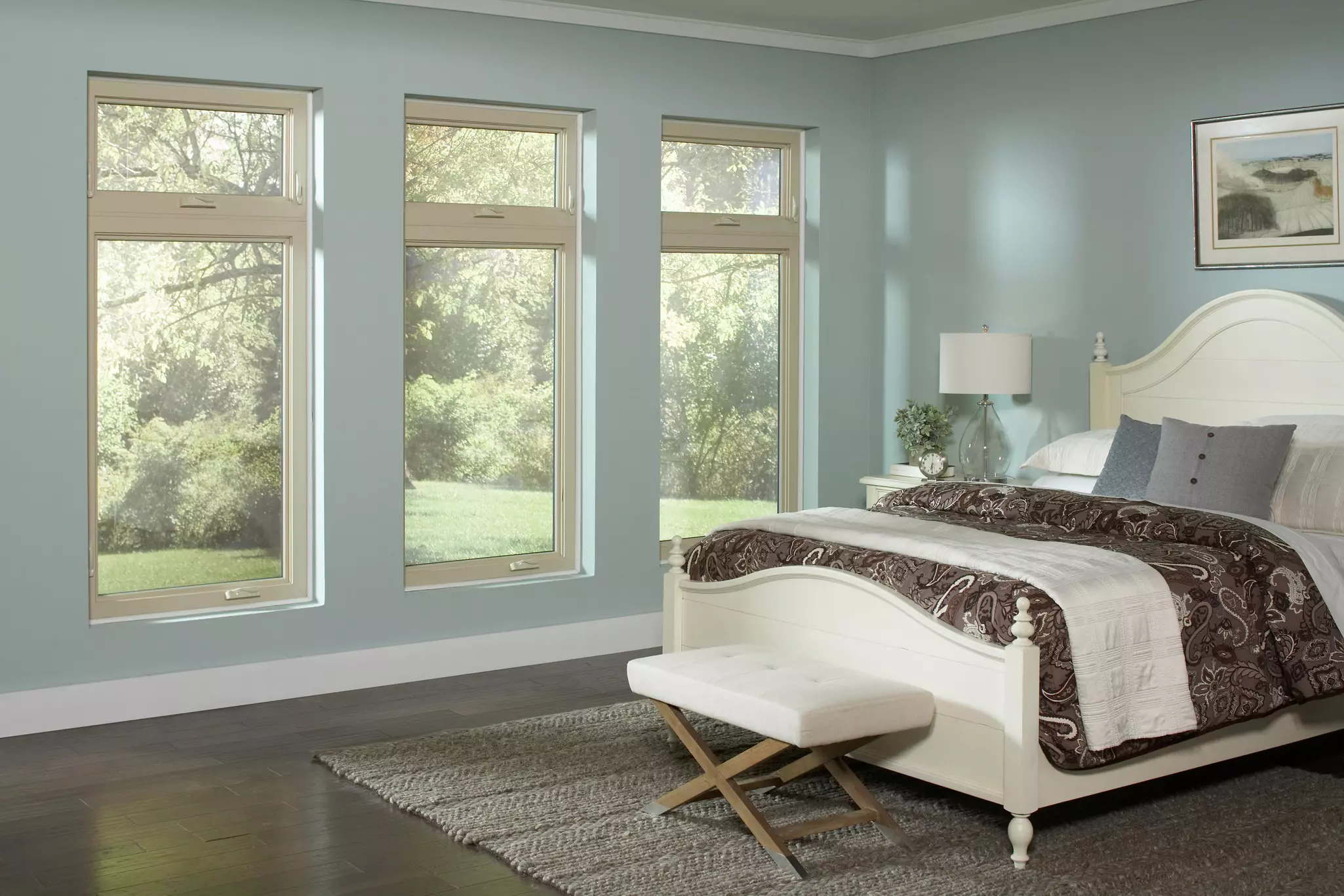 A light blue bedroom with a wall of casement and awning windows overlooking a green yard.