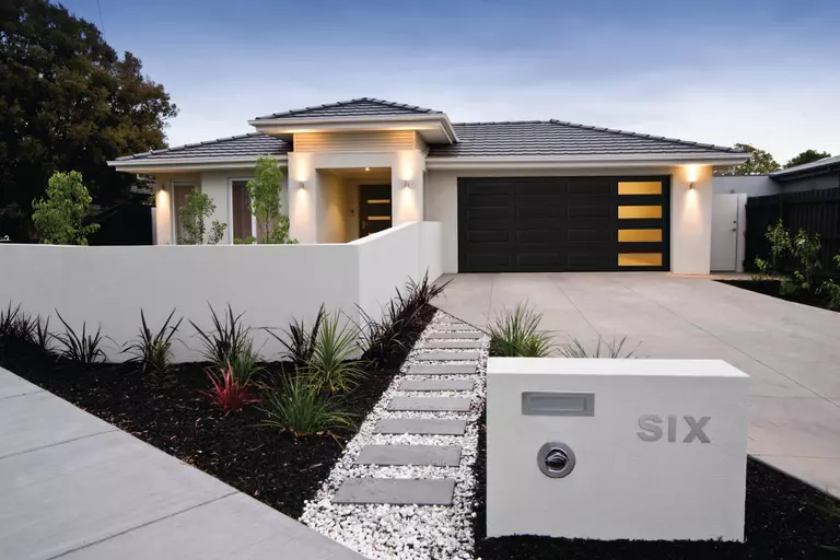 A modern home with a sleek, four-windowed garage door. A small gravel path leads to the driveway.