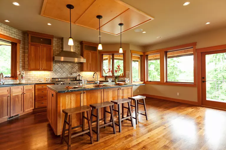 A large, open kitchen of a log cabin home that has wood cabinets, floors, and trim on the large energy-efficient windows of the home.