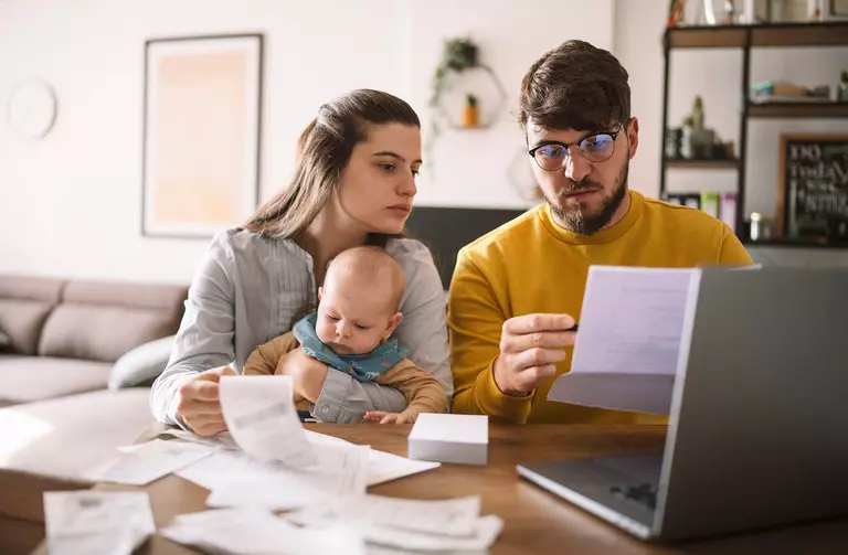 A husband, wife, and their baby at the table reviewing bills and expenses from their home remodel together. 