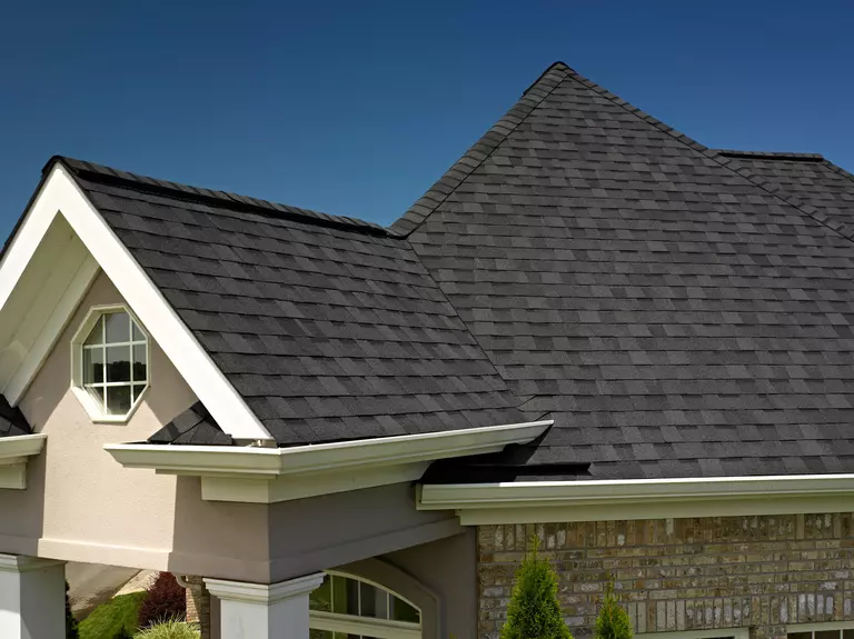 Roof of a home with black shingles and an off-white exterior.