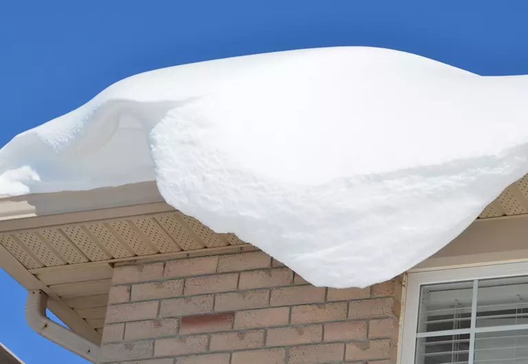 Heavy snow piled up on a roof and pouring over into the gutters, causing roof damage
and ice dams.