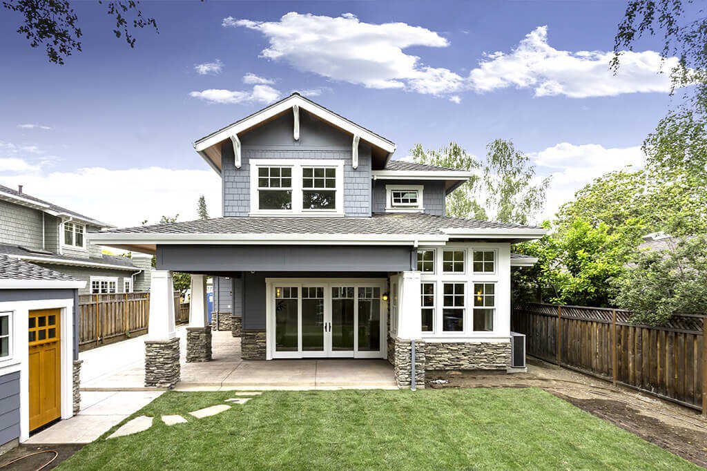 The back of a blue craftsman-style home with sliding patio doors leading to a fenced in backyard with a shed.