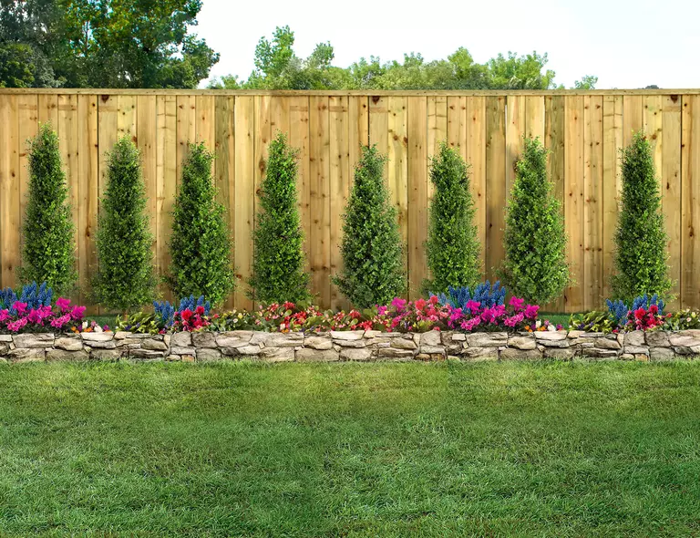 A privacy wall built in the backyard of a home with plants and flowers planted around it.