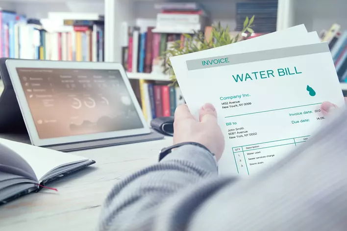 A person at their desk in their book-filled office looking at the invoice for their water bill.