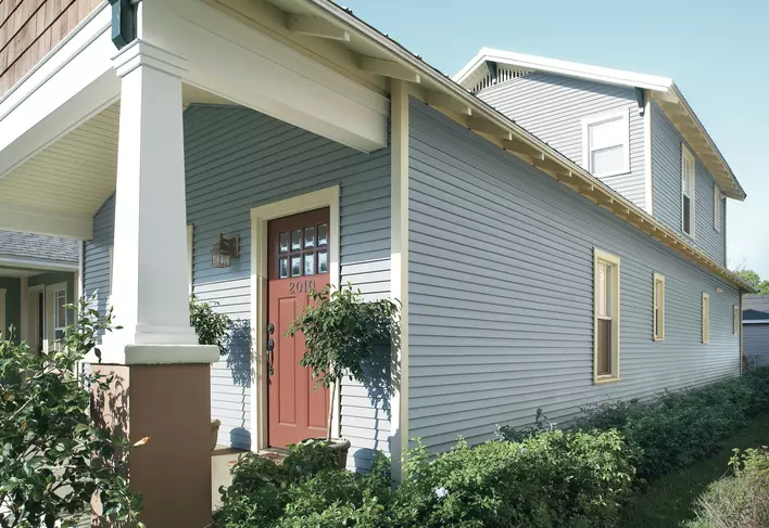 Side view of a home with a red door and light blue insulated vinyl siding