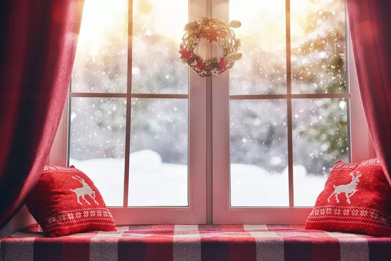 A windowsill decorated with festive pillows and a wreath above.