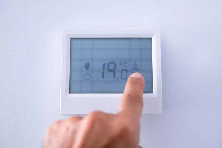 A person taps the display of their home’s programmable thermostat. Programmable thermostats are a great way to save energy and money and keep your home comfortable in the summer.