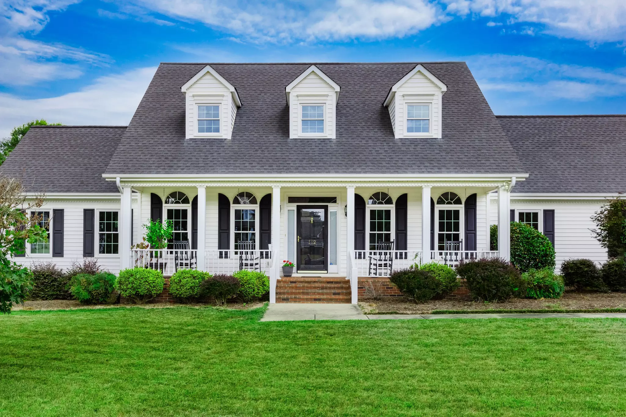 Front of a two-story home with white windows with grids and black shutters and doors.