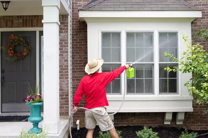 A person spraying down windows with a water hose on the exterior of a home