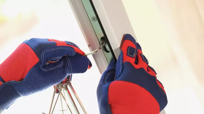 A person wearing work gloves using an hex-key wrench to adjust the balance of a window that won’t stay up.