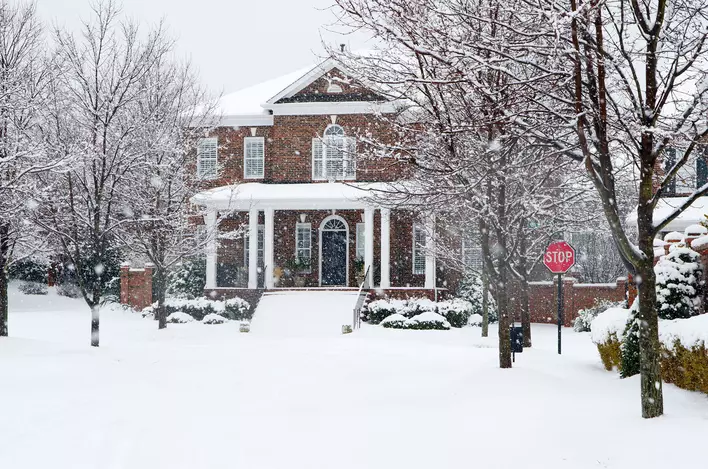 Street view of a large house while it is snowing