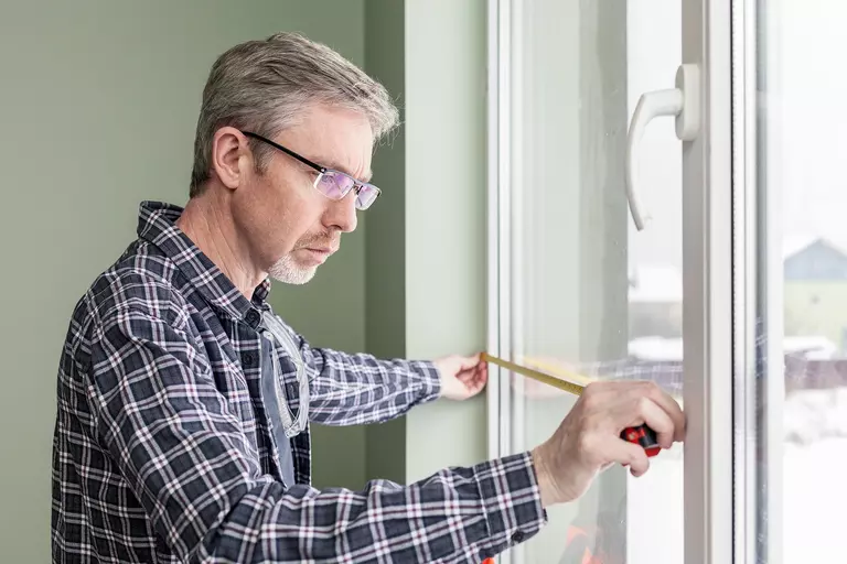 Man using a tape measure to determine the width of a casement window.