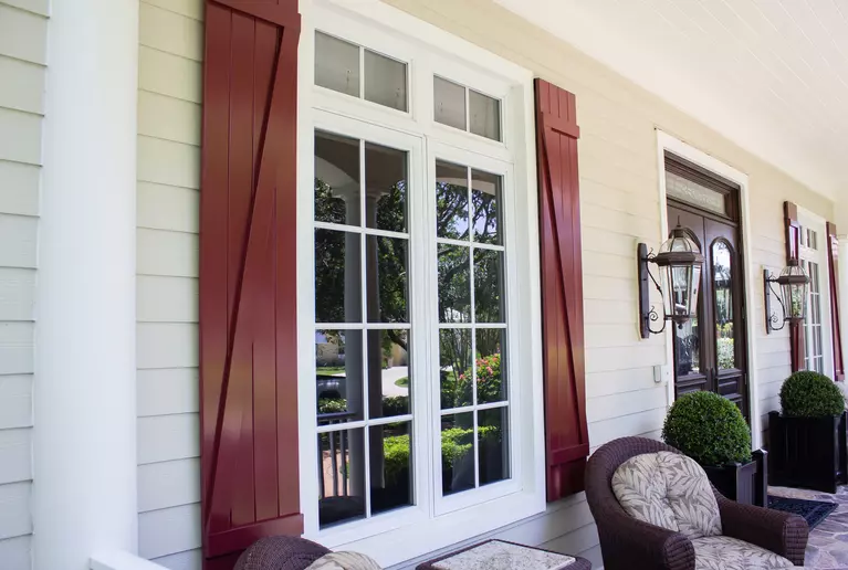 The porch of a home with red-brown board and batten shutters.
