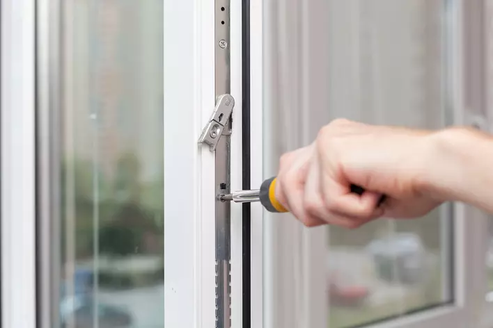 A person using a screwdriver to adjust the balances on an old window that won’t stay up.